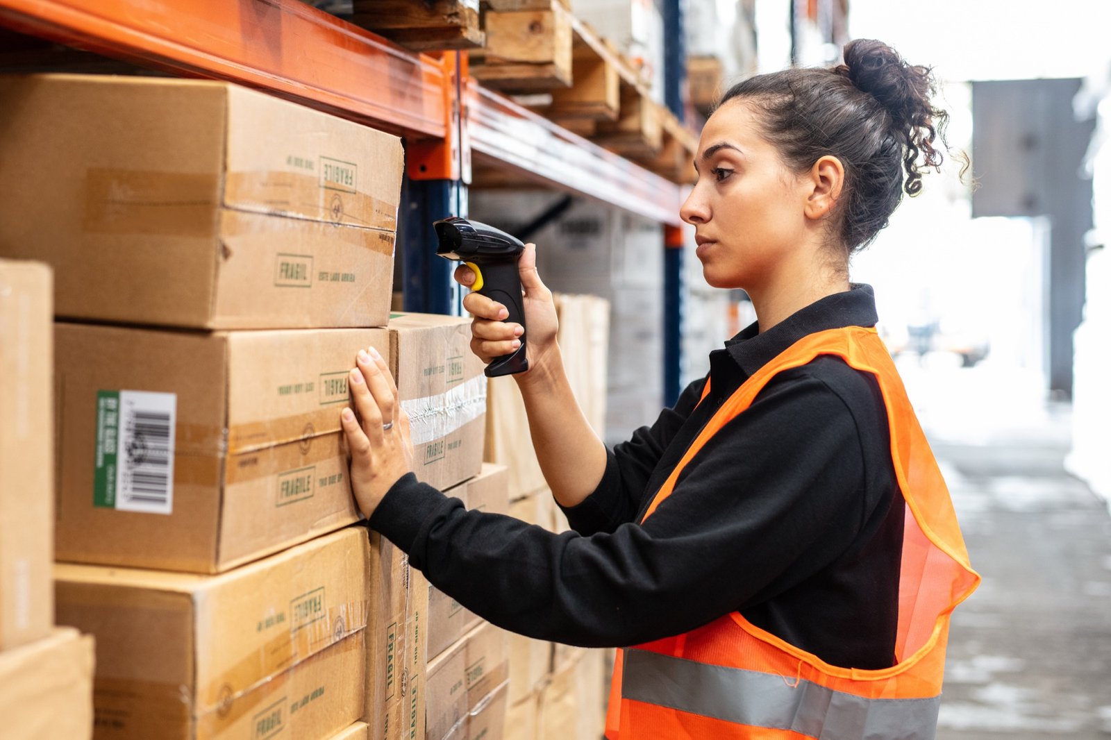 A warehouse worker in a hi-vis vest scanning boxes on a shelf