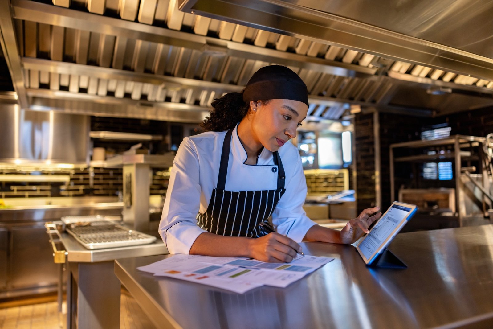 A kitchen worker reviewing paperwork on a stainless steel counter